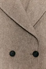 Abrigo largo cruzado color gris oscuro, confeccionado con lana. Presenta cuello solapa, manga larga, bolsillos delanteros de plastrón y cierre frontal con botones.