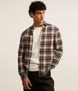 Camisa de flanela con estampado a cuadros en tonos beige, azul y rojo. Presenta cuello clásico, cierre frontal con botones y mangas largas con puños abotonados.