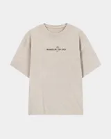Remera oversize color beige de corte holgado, con estampa en la espalda que representa un esqueleto dentro de un ataúd con rayos oscuros y texto descriptivo.