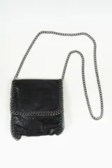 Bandolera pequeña de color negro con acabado texturizado y detalles de costuras reforzadas en los bordes. Cuenta con una correa larga de cadena metálica en tono oscuro.