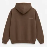 Canguro con capucha de calce oversize, confeccionado en tejido pesado color gris claro. Presenta un bordado minimalista con la palabra 'ASCEND' en la parte superior trasera, puños y ruedo acanalados.