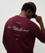 Remera de corte oversized color bordó, con cuello redondo y manga corta. Presenta un estampado en la espalda con lettering manuscrito que incluye las ciudades Paris, Tokyo y New York, junto con detalles tipográficos adicionales.