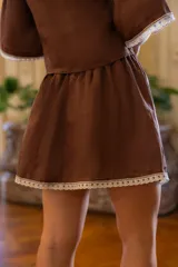Falda corta color marrón, confeccionada en lino, con detalle de puntilla cruda en el ruedo y cintura elástica.