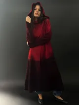 Tapado rojo con capucha, confeccionado en lana merino teñida con técnica tie-dye. Tiene corte recto, largo, bolsillos laterales y cierre cruzado con broches a presión ocultos.