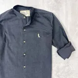 Camisa gris oscura de algodón con cuello mao, manga larga con puños enrollados, cierre frontal con botones y logo bordado en el pecho.