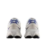 Championes urbanos New Balance modelo 9060, con diseño futurista inspirado en la estética de los años 2000. Presentan una combinación de tonos beige y blanco con detalles en azul, entresuela esculpida con tecnología de amortiguación ABZORB y SBS, y una capellada de materiales mixtos.