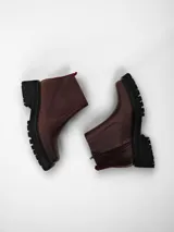 Bota corta de cuero marrón con suela track negra, cierre lateral y detalle de tira de tela roja en la parte trasera.