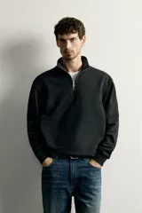 Sudadera negra de corte regular fit, con cuello subido, cierre frontal de cremallera corta y acabados en rib elástico en puños y cintura.