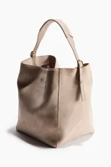 Cartera tipo shopper de gamuza color beige, con diseño estructurado, asa superior ajustable y herrajes metálicos dorados.