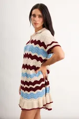 Vestido corto de tejido de punto con diseño de ondas en colores beige, bordó y celeste, con cuello polo y cierre frontal parcial con botones. Presenta mangas cortas y volado en el ruedo.