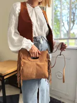 Cartera bandolera de cuero color camel, con forro interno de tela y flecos laterales.