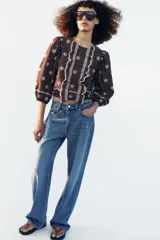 Blusa azul marino con estampado de lunares blancos, cuello redondo y mangas abullonadas. Presenta detalles de bordados perforados, volantes delanteros y acabados elásticos.