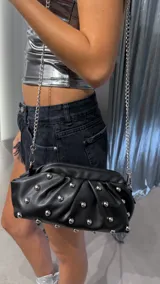 Cartera negra con frunces y tachas plateadas, con correa de cadena metálica.