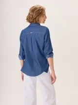 Camisa de algodón color gris claro, con cuello clásico y detalle de volados en la cartera frontal. Presenta mangas largas con puños abotonados y un corte recto.