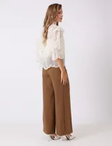 Blusa de tul bordado color beige, marca Liv Los Angeles, con cuello alto, cierre frontal de botones y mangas ¾ amplias con volados.