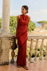 Vestido largo color caldera, sin mangas, con escote redondo y drapeado en el cuello. Presenta un detalle de volados con flecos en diagonal a lo largo del cuerpo.