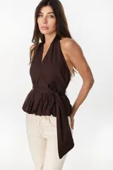 Blusa de cuello halter en color beige, con escote en V pronunciado, corte ajustado en el torso y detalle de volados fruncidos en la cintura con un lazo lateral ajustable.