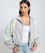 Campera corta viento de mujer de la marca Blue Steel, con cuello alto, mangas largas con puños elásticos y cierre frontal por cremallera. Presenta recortes contrastantes en tonos gris, celeste y amarillo pastel, y ruedo corto con elástico. Confeccionada en poliamida, un tejido sintético ligero y suave.