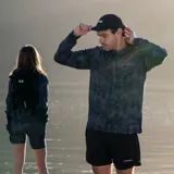 Campera cortaviento con capucha, estampado camuflado en tonos grises y logo Merrell en el pecho. Cierre frontal con cremallera y bolsillos laterales. Ideal para trail running.