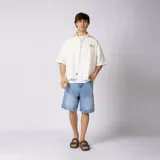Camisa de manga corta color marfil, corte boxy, con cuello camisero, cierre frontal de botones y pequeño bordado marrón en el pecho con las siglas VCP.