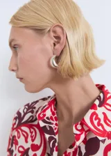 Camisa de corte recto y diseño holgado, confeccionada en algodón con estampado floral en tonos rojos y bordó sobre fondo crudo. Presenta cuello camisero clásico, cierre frontal con botones y mangas largas.