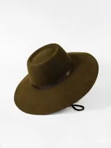 Sombrero de ala ancha color marrón, confeccionado en lana, con cinta decorativa y detalle de placa metálica con logo en el lateral.