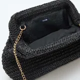 Bolso tipo clutch de estructura rígida, tejido en rafia color negro, con cierre superior y cadena metálica dorada para llevar al hombro.