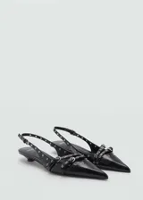 Zapato de charol negro con punta fina, escote asimétrico, tira trasera con hebilla ajustable y detalle de troquelado y apliques metálicos. Tacón kitten.