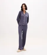 Pijama de dos piezas estilo americano en color azul grisáceo. La blusa es de manga larga con cuello solapa, cierre frontal de botones y detalle de bies en contraste. El pantalón es de corte recto con cintura elástica y detalle de bies en el ruedo.
