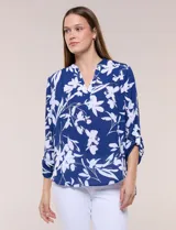 Blusa de gasa de calce suelto y caída ligera, color azul con estampado floral blanco. Presenta escote en V con cuello mao, tabla central, mangas largas regulables con presilla y botón, ruedo redondeado de estilo mullet y espalda con canesú y pliegue central.
