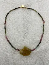 Collar de cuentas pequeñas facetadas de piedras naturales en tonos verdes, rosados y negros, con un dije central de piedra irregular en tono ocre.