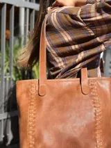 Cartera tipo tote de cuero color camel, con diseño estructurado, costuras decorativas laterales y doble asa superior para el hombro.