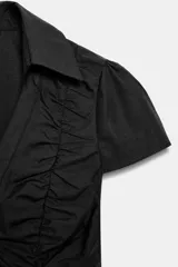 Top de cuello solapa y escote en pico, con manga corta y cierre frontal con botones. Presenta un diseño ajustado con detalles de frunces en el delantero.