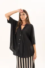 Camisa negra de corte oversize con diseño de encaje calado, escote en V, cierre frontal con botones y mangas tres cuartos. Presenta un diseño asimétrico con la parte posterior ligeramente más larga.