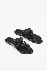 Sandalia plana de cuero negro con diseño de tiras trenzadas que cruzan el empeine y se sujetan entre los dedos. Presenta costuras decorativas en el borde de la plantilla y suela plana.