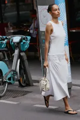 Vestido midi de color blanco con cuello redondo y manga sisa, confeccionado con un diseño combinado que presenta un cuerpo de tejido liso y una falda vaporosa con cintura elástica fruncida y cordón ajustable.