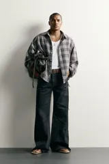 Camisa de algodón con corte boxy fit, diseño a cuadros en tonos grises y blancos, cuello clásico y manga larga con puños abotonados.