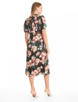 Vestido midi de satén con estampado floral sobre fondo negro. Presenta cuello a la base con frunce, mangas cortas abullonadas con terminación elástica, cintura definida y un tajo lateral pronunciado. Incluye forro interno y lazo posterior para ajustar el cuello.