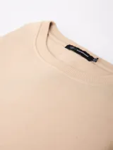 Buzo de felpa color beige, de cuello redondo y mangas largas con puños acanalados.