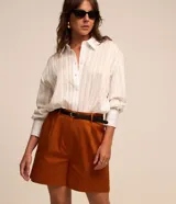 Short de sastrería color beige, de corte recto con pinzas delanteras y trabillas en la cintura. Incluye un cinturón de poliuretano a tono con hebilla metálica dorada.