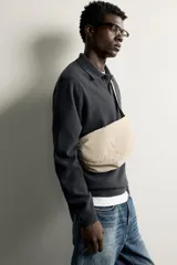Bolso de hombro de nylon color negro, con diseño curvo y cierre de cremallera en el compartimento principal. Cuenta con asa ajustable para llevar al hombro y bolsillo interior con cierre.
