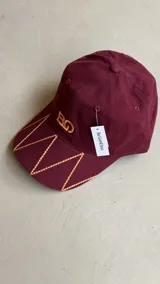 Gorra negra con bordado de las iniciales BG en el frente y diseño de costuras geométricas en la visera.