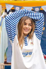 Remera tipo polo de manga larga con diseño de mangas raglán a rayas horizontales azules y blancas. El cuerpo de la prenda es blanco, con cuello polo y una pequeña estampa en el pecho. Confeccionada en tejido de algodón con spandex.