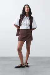 Short pollera de tiro medio con silueta recta y diseño tipo falda en el frente, confeccionado en tela de sastrería color marrón.