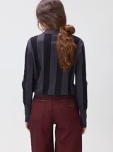 Sweater de punto con diseño de rayas verticales en tonos negro y gris oscuro. Presenta cuello alto tipo polera, mangas largas con puños ajustados y ruedo elástico. Incluye un pequeño bordado en color rojo en el pecho.