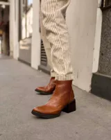 Botinetas de cuero vacuno con textura tipo reptil en color marrón chocolate. Presentan un diseño de caña media con cierre posterior, puntera redondeada y suela de goma con taco cuadrado robusto.