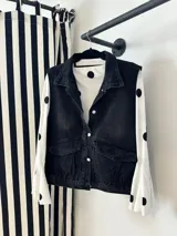 Chaleco de denim negro con cierre frontal de botones metálicos, cuello camisero y dos bolsillos frontales con solapa.