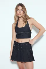 Minifalda plisada de denim oscuro, con detalles de tachas plateadas distribuidas en los pliegues y el cuerpo de la falda.