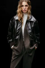 Pantalón sastrero de tiro alto, color marrón oscuro con finas rayas verticales blancas. Presenta cierre frontal con botón oculto y corchetes, bolsillos al bies y bolsillos decorativos traseros. Las piernas son rectas y tienen pliegues marcados al frente y atrás.