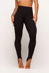Calza legging de tiro alto color negro, confeccionada en tejido técnico de poliamida y elastano. Presenta un diseño minimalista con ajuste al pie mediante tira elástica (estribo).